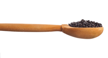 Black lentils in the wooden spoon isolated on a white background.