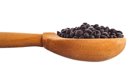 Black lentils in the wooden spoon isolated on a white background.