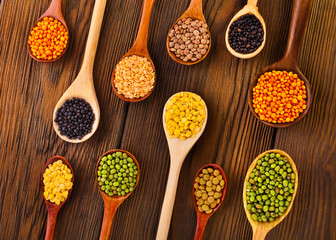 Various lentils in the wooden spoons on a wooden background. Top view.