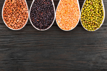 Bowls of various lentils on a wooden background. Top view. Copy space.