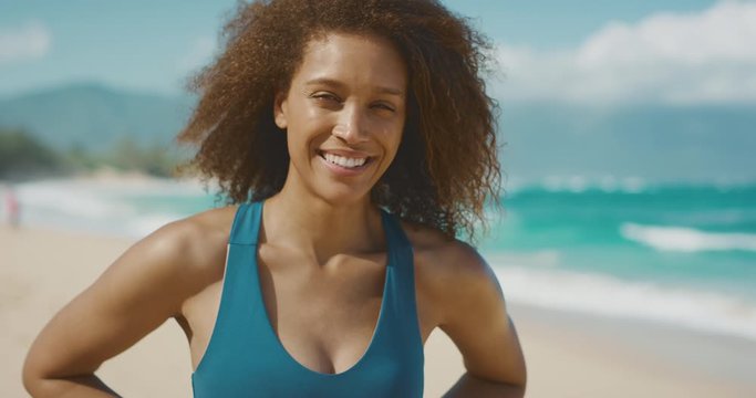 Portrait of a beautiful young african american woman in a blue sports bra smiling and looking radiant at the beach after her morning workout, women's health and fitness concept