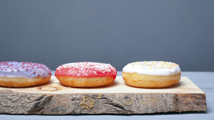 multicolored assorted red,white,violet donuts coated with glaze and sprinkled with Easter powder on a wooden stand on a gray background, sweet eco food.