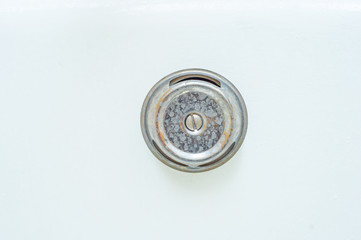 The overflow hole in the bathroom is covered with an iron cover dirty in smudges and rust.
