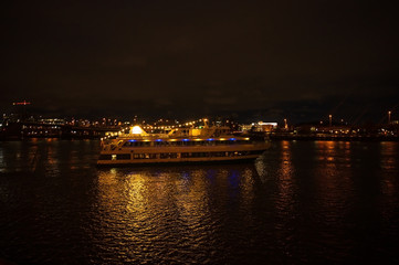 Fototapeta na wymiar Night pleasure boat, or yacht for a walk with people. Night city with a river and a big boat