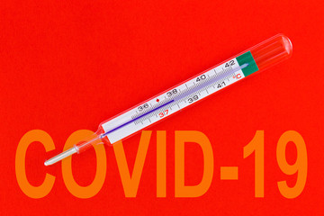 Traditional medical thermometer for measuring body temperature on a red background with word -  covid 19 . Thermometer display 37.9 degrees celsius