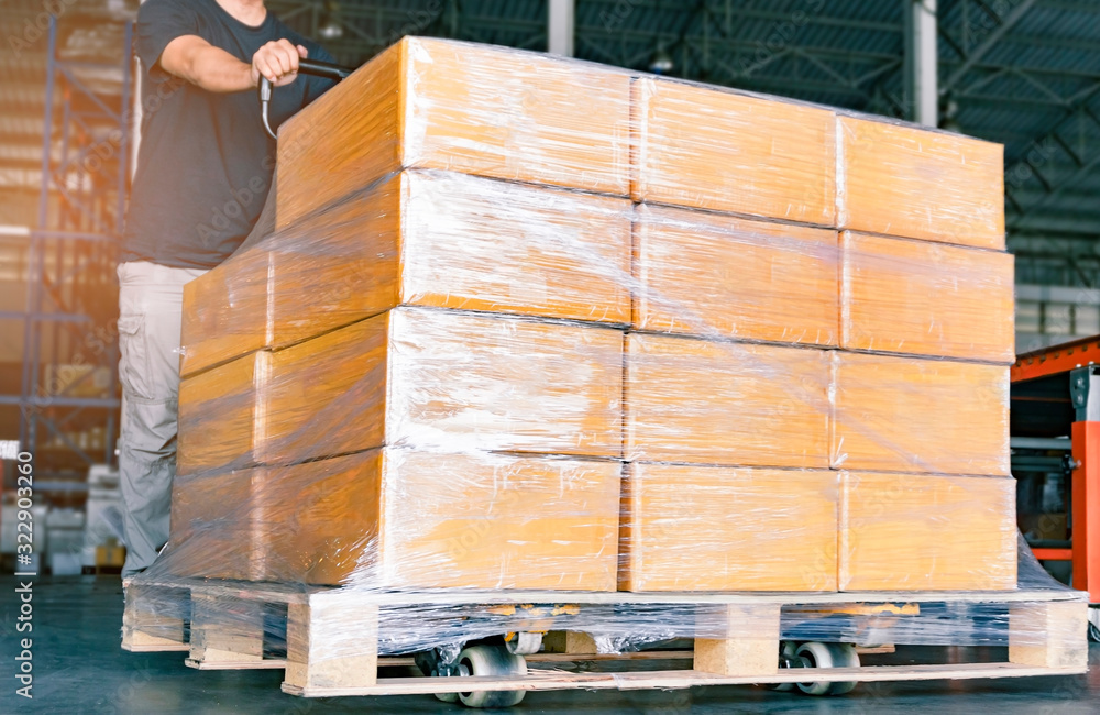 Wall mural worker working with hand pallet truck unloading shipment goods in warehouse, cargo export, courier d