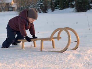 Child (little boy) enjoying sledding, pushing a wooden sled. Winter fun, activities for kids, childhood memories. Wintertime, sunny cold weather, snow, sunset