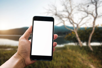 A man hand holding smart phone device in the mountains and blurred background of trees in the forestt