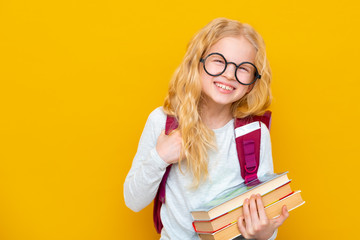 Back to school. Portrait of blonde school girl in round glasses with bag and books. Yellow studio background. Education. smiling at camera. Copyspace.