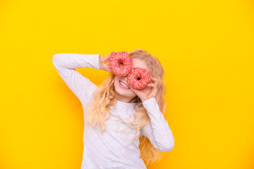 Crazy cheerful blonde girl in birthday hat smiling, having fun and looking through two red donuts...