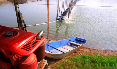 Obraz premium Selective focus at orange motor engine on foreground with blurred blue boat and aerator multiple turbine wheels on water surface for increase oxygen in shrimp pond and natural farm background 
