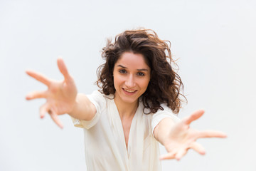 Smiling young woman with outstretched hands want to embrace. Cheerful curly lady looking at camera. Invite concept