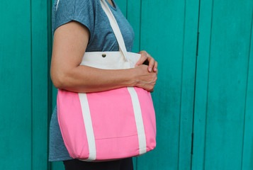 Closeup of modern designed white and pink reusable cotton bag carrying by Asian woman with vintage wooden wall background. 