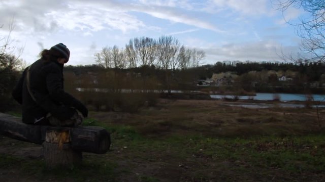 Man sitting on a bench near a scenic river to enjoy some solitude and fresh air outside. Wide back view.