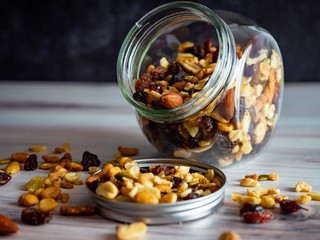 Glass jar full of healthy, good carbohydrate packed nuts, raisins and seeds spilling out onto the table.