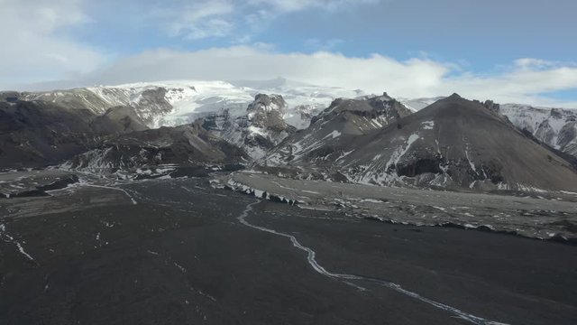 Drone shot flying towards a mountain in Iceland over a black sand beach with a small river