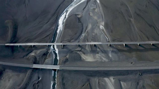 Looking down on a bridge in Iceland running over flat black lava sand across a glacial runoff river