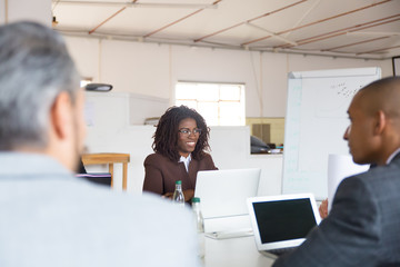 Smiling African American woman sitting at morning meeting. Cheerful manager with dreadlocks listening colleagues. Business meeting concept