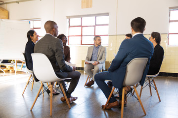 Focused managers sitting in chairs with paper documents. Confident office employees during meeting....