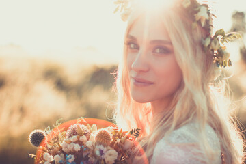 Beautiful young woman portrait in a white dress in boho style with a floral wreath in the summer in the field. Selective soft focus. © Roman