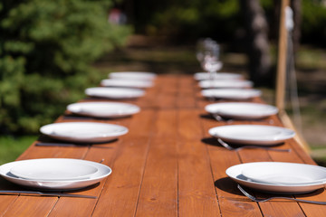 White plates are placed on a wooden table in the park on a green lawn.