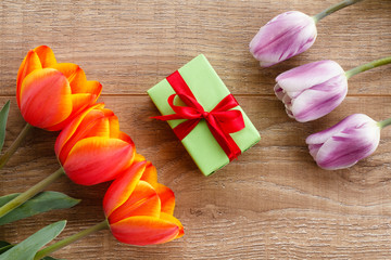 Gift box with red ribbons and tulips on wooden boards .