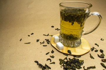  Glass cup of green tea on a stand with sprinkled green tea and sugar cubes