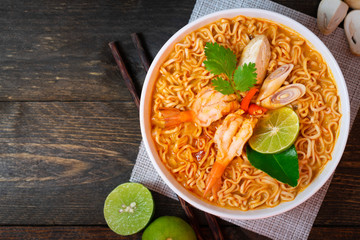 Noodle in spicy soup with shrimp and mushroom in white bowl on wooden table.