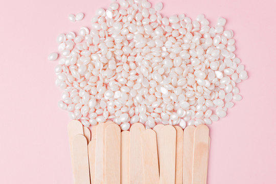 Wax for depilation of white pearl color and wooden stick spatula on pink background. Concept of waxing, smooth skin, bodycare, spa salon industry. Banner copy space, flyer, coupon