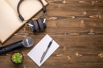 Microphone, headphone, book and paper note on brown wooden board. Learning about speaking concept