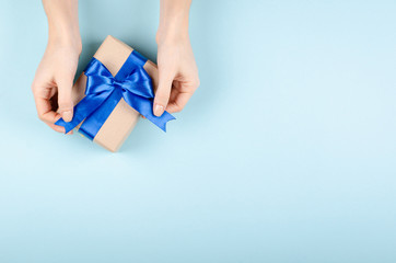 Hands with gift box on blue background composition, present with ribbon and bow.