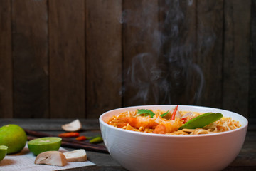 Noodle in spicy soup with shrimp and mushroom in white bowl on wooden table, Steam and Smoke.
