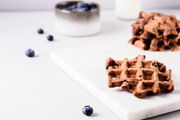 Homemade Chocolate waffles, milk and blueberries on white marble tray. Breakfast. Selective focus