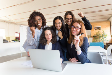 Group of successful businesswomen with raised fists with laptop. Professional office managers posing near table with laptop. Business success, teamwork concept