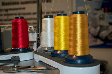Spools of thread in working condition on sewing equipment. Color is yellow, white, red. Manufactory concept.