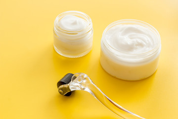 Dermaroller for home cosmetologic procedure near creams on yellow background