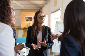 Group of young women standing in circle and discussing project. Smiling creative business team talking in office. Teamwork concept