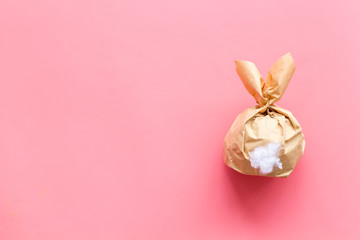 Easter gift in shape of bunny with tail on pink background top-down copy space