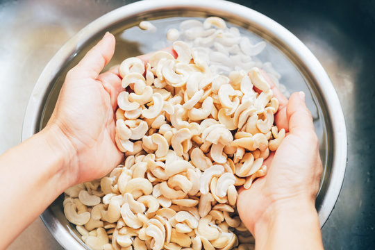 Closeup, woman&rsquo;s hands wash, scrub, soak and scoop cashew nuts from water in bowl to remove dirts, tannins, phytic acid on surface, healthy & good for digestion of plant based diet, vegan, vegetarian.