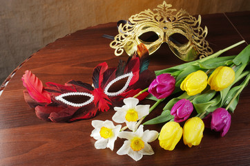 Carnival masks, a bouquet of daffodils and tulips on a wooden table.