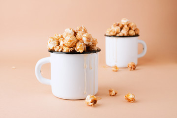 Caramel popcorn in vintage white metal cups on a brown background