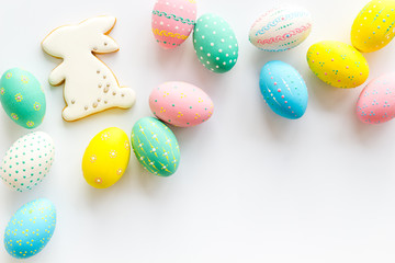 Easter symbols. Painted eggs and bunny gingerbread on white desk top-down frame copy space