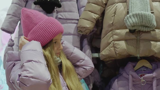 Cute little girl trying on new pink hat. Nice girl wearing winter clothing adjusting knitted hat on head. Shopping concept