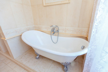 Classic bathroom in beige tones. Curved bath tub. Large beige tile. White tiles on the floor....