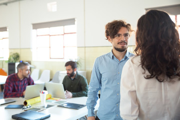 Confident bearded man in eyeglasses talking with woman. Two coworkers communicating in open space office. Communication concept