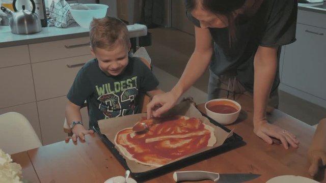 Mutter und Sohn streichen Tomantensauce auf Pizza
