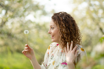 Pretty girl blowing dandelion in summer park. Green grass beautiful nature. Pure emotion.