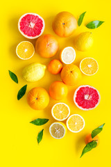 Fresh citrus background. Oranges, grapefruits, leaves - whole fruits and halfs - on yellow background top-down