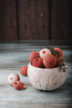 Litchi chinensis with copy space. Fresh litchi fruits in a bowl in old rustic wooden background. Raw red organic lychee fruit ready to eat.