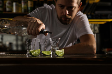 Bartender pouring Mexican Tequila into shot glass at bar counter, closeup